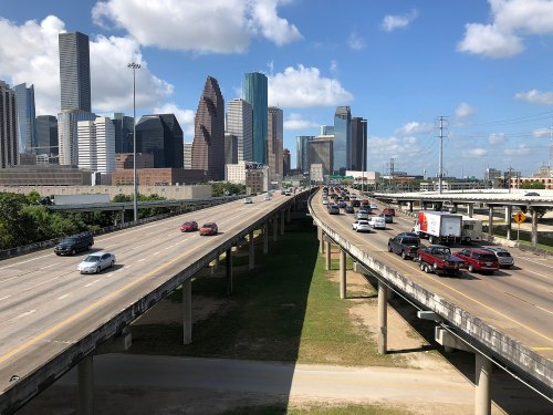 A busy highway with cars, leading towards a skyline of tall buildings under a partly cloudy sky.