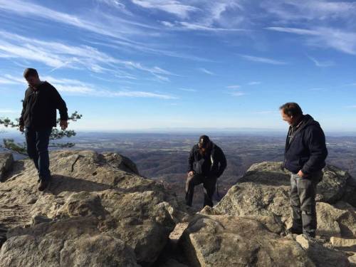 Three people exploring rocky terrain on a mountain with a scenic view of the landscape below.
