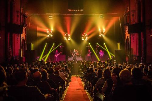 A lively concert scene with a band performing on stage, colorful lights illuminating the audience in a packed venue.