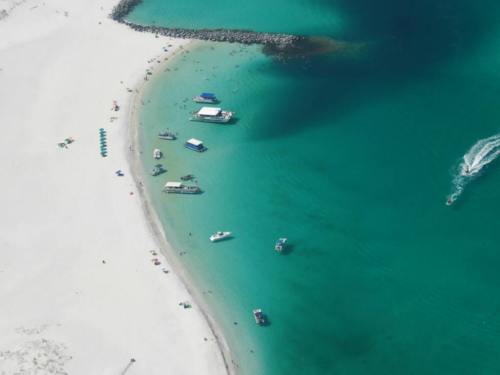 Aerial view of a beach with turquoise water, boats, and people enjoying the sun on a sandy shore.