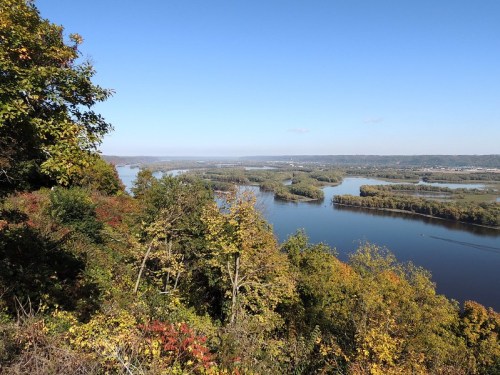 A scenic view of a river winding through lush, colorful trees under a clear blue sky.