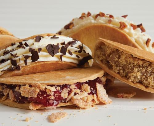 A close-up of dessert tacos filled with various sweet fillings, including fruit, cream, and crumbled toppings.