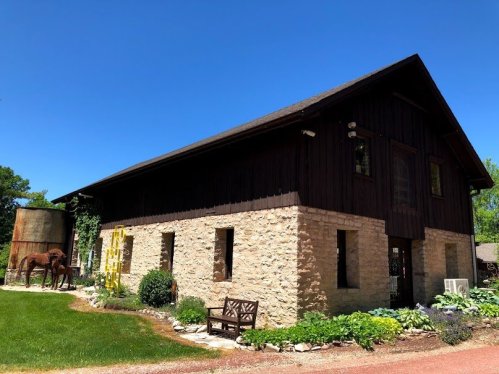 A rustic two-story building with a stone and wooden exterior, surrounded by greenery and a clear blue sky.