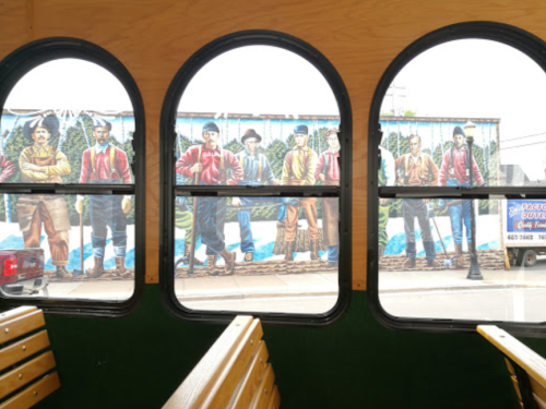 View from inside a trolley, showing a colorful mural of men in historical attire outside the window.