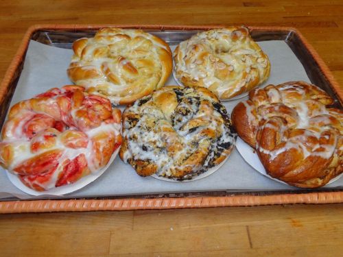 A tray of five sweet, glazed pastries in various flavors, including strawberry, poppy seed, and cinnamon.