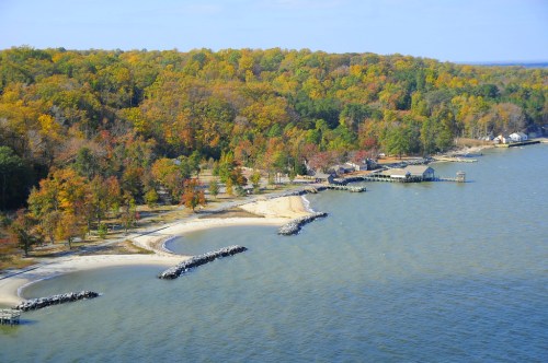 Aerial view of a shoreline with sandy beaches, rocky outcrops, and colorful autumn trees along the water's edge.