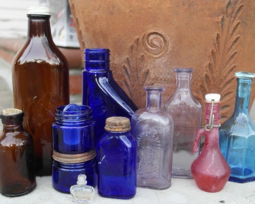 A collection of vintage glass bottles in various shapes and colors, including brown, blue, and purple, against a textured background.