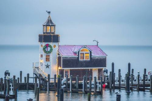 A charming waterfront building decorated with lights and a wreath, surrounded by a calm sea and docked boats.
