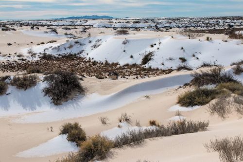 A vast desert landscape with rolling sand dunes and sparse vegetation under a cloudy sky.
