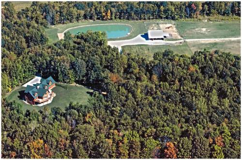 Aerial view of a wooded area featuring a large house, a pond, and a barn on a grassy landscape.