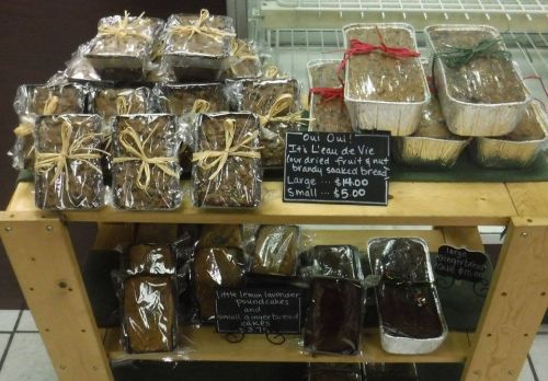 A display of wrapped baked goods, including fruit and nut cakes, on a wooden shelf with price signs.
