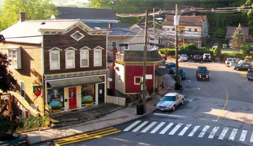 A quaint town intersection with shops, parked cars, and power lines under a clear sky.