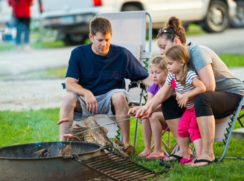 A family gathers around a campfire, roasting hot dogs while enjoying a summer evening outdoors.