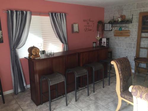 A cozy home bar with a wooden counter, stools, and decorative curtains against a pink wall.