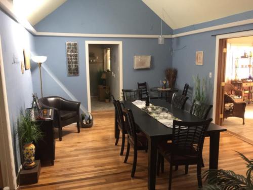 A cozy dining area with a large table, black chairs, and blue walls, featuring plants and a lamp.