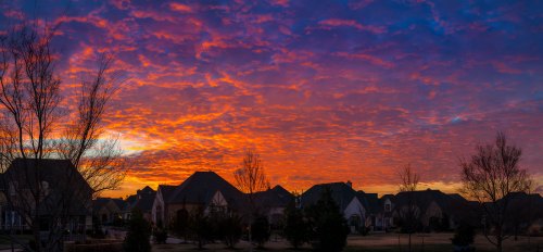 A vibrant sunset paints the sky in shades of orange and purple over a suburban neighborhood with silhouetted houses.