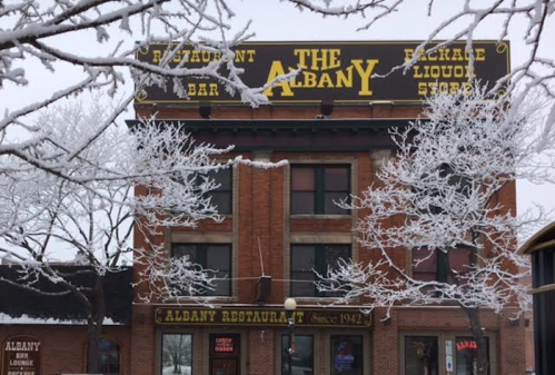 The Albany building with snow-covered trees, featuring a restaurant, bar, and liquor store sign.