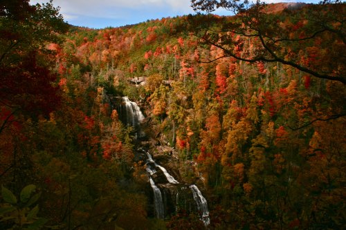 A scenic view of a waterfall surrounded by vibrant autumn foliage in shades of orange, red, and yellow.