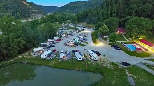 Aerial view of a campground with RVs, cars, and a pool, surrounded by trees and hills.