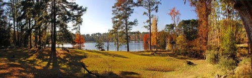A serene lake surrounded by trees with autumn foliage, reflecting a clear blue sky in a peaceful landscape.