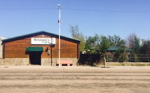 A rustic wooden café building with a sign reading "Brianna's Café," surrounded by trees and a clear blue sky.
