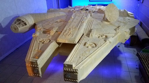 A large, detailed wooden model of a spaceship, resembling the Millennium Falcon, displayed in a well-lit room.