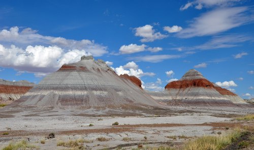 Colorful striped rock formations under a blue sky with fluffy clouds in a desert landscape.