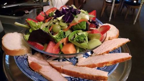 A colorful salad with mixed greens, fruits, and sliced chicken, served with pieces of bread on a decorative plate.