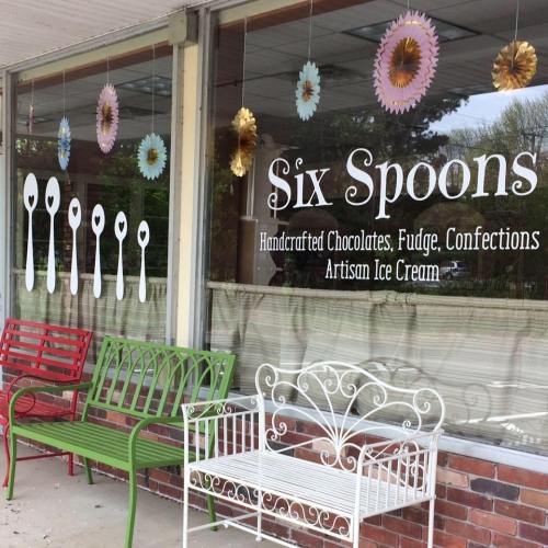 Storefront of "Six Spoons" featuring colorful benches and a sign for handcrafted chocolates and artisan ice cream.