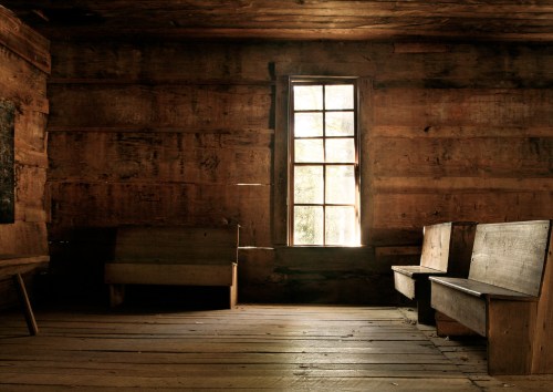 A rustic, dimly lit room with wooden walls, a window, and simple wooden benches.