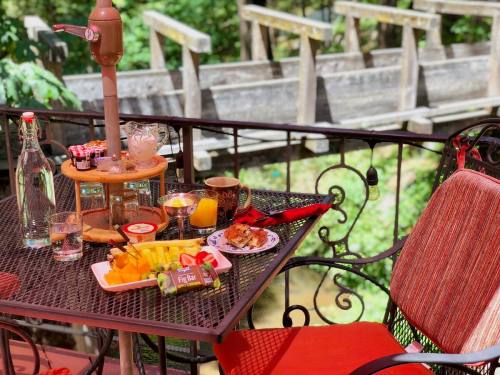 A cozy outdoor table set with a fruit platter, drinks, and a dessert, overlooking a wooden bridge and greenery.