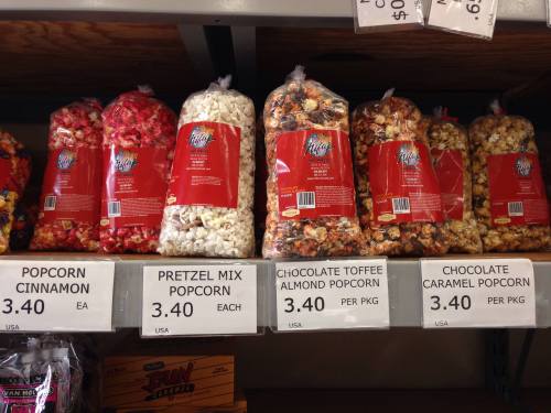 Bags of various flavored popcorn, including cinnamon, pretzel mix, toffee almond, and caramel, displayed on a shelf.