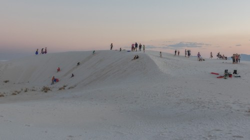 People enjoying a sandy landscape at dusk, with gentle hills and a pastel sky in the background.