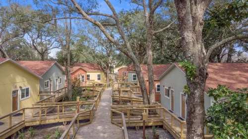 Colorful cottages surrounded by trees, connected by wooden walkways in a serene outdoor setting.