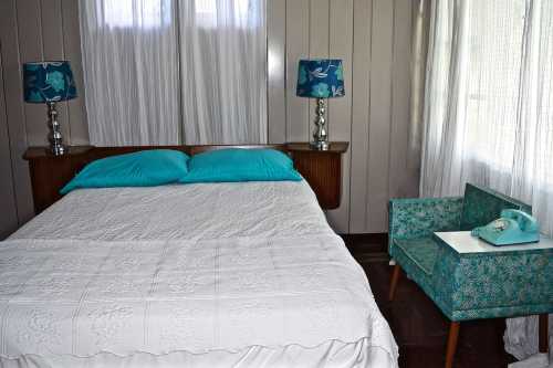 A cozy bedroom featuring a bed with turquoise pillows, patterned lamps, and a vintage phone on a side table.