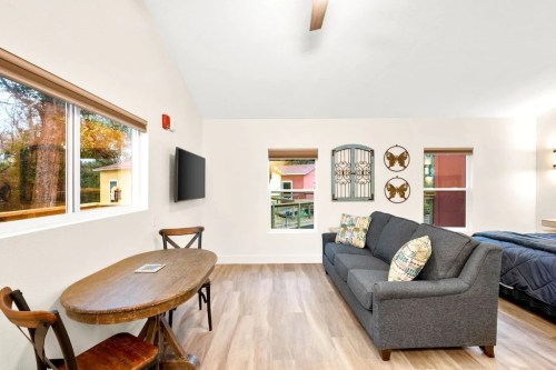 Cozy living space with a sofa, dining table, TV, and large windows overlooking trees. Modern decor and warm lighting.