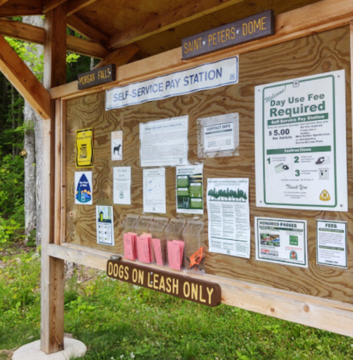 A wooden kiosk displaying park information, fee details, and a notice for dogs on a leash.