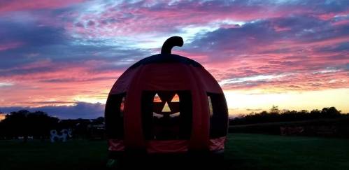 A large pumpkin-shaped structure with a carved face silhouetted against a vibrant sunset sky.