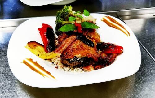 A beautifully plated dish featuring fish, rice, plantains, broccoli, and garnishes of peppers and herbs.