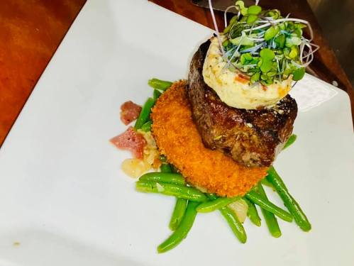 A gourmet dish featuring a beef patty atop a crispy base, garnished with microgreens and served with green beans.