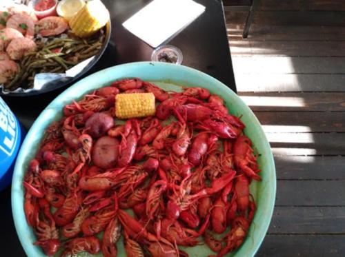 A large platter filled with red crawfish and a piece of corn, set on a wooden table.
