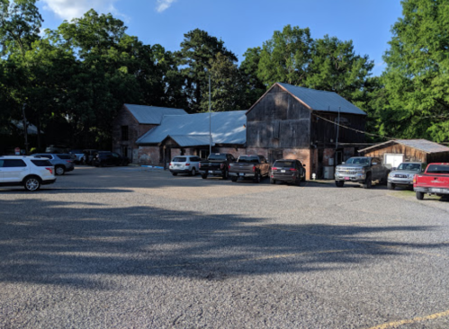 A rustic building with a metal roof surrounded by parked cars and trees under a clear blue sky.