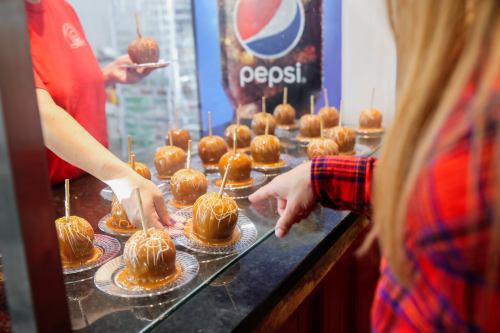 A person points at caramel apples displayed in a glass case, with another hand reaching for one. Pepsi logo in the background.