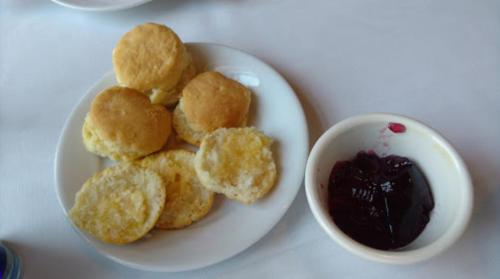 A plate of golden biscuits next to a small bowl of dark berry jam.