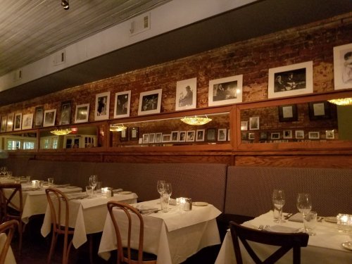 Cozy restaurant interior with wooden tables, elegant lighting, and framed black-and-white photos on exposed brick walls.