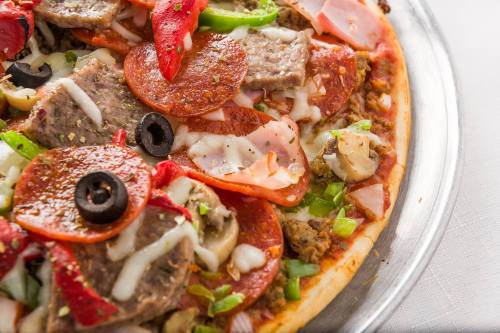 Close-up of a pizza topped with pepperoni, green peppers, olives, mushrooms, and various meats on a golden crust.