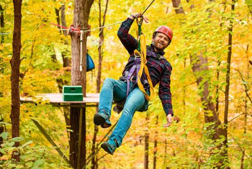 A person in a helmet zip-lining through a colorful autumn forest, smiling as they enjoy the adventure.