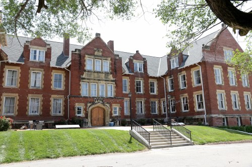 Historic brick building with large windows, a central entrance, and landscaped greenery in front.