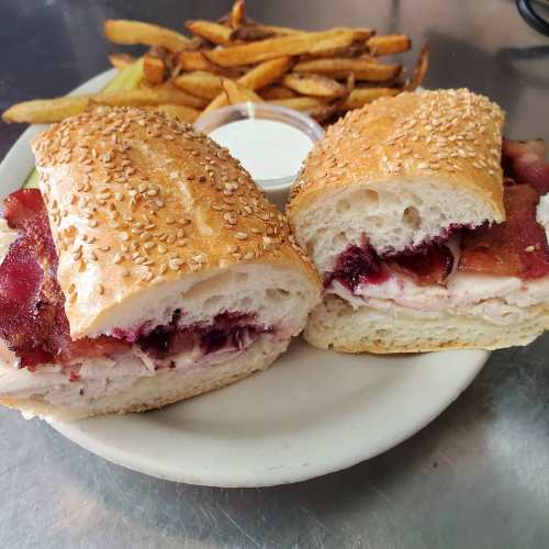 A sesame seed bun sandwich filled with turkey and bacon, served with fries and a side of dipping sauce.