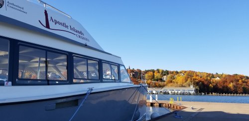 A boat docked at a marina with autumn foliage in the background and clear blue skies.
